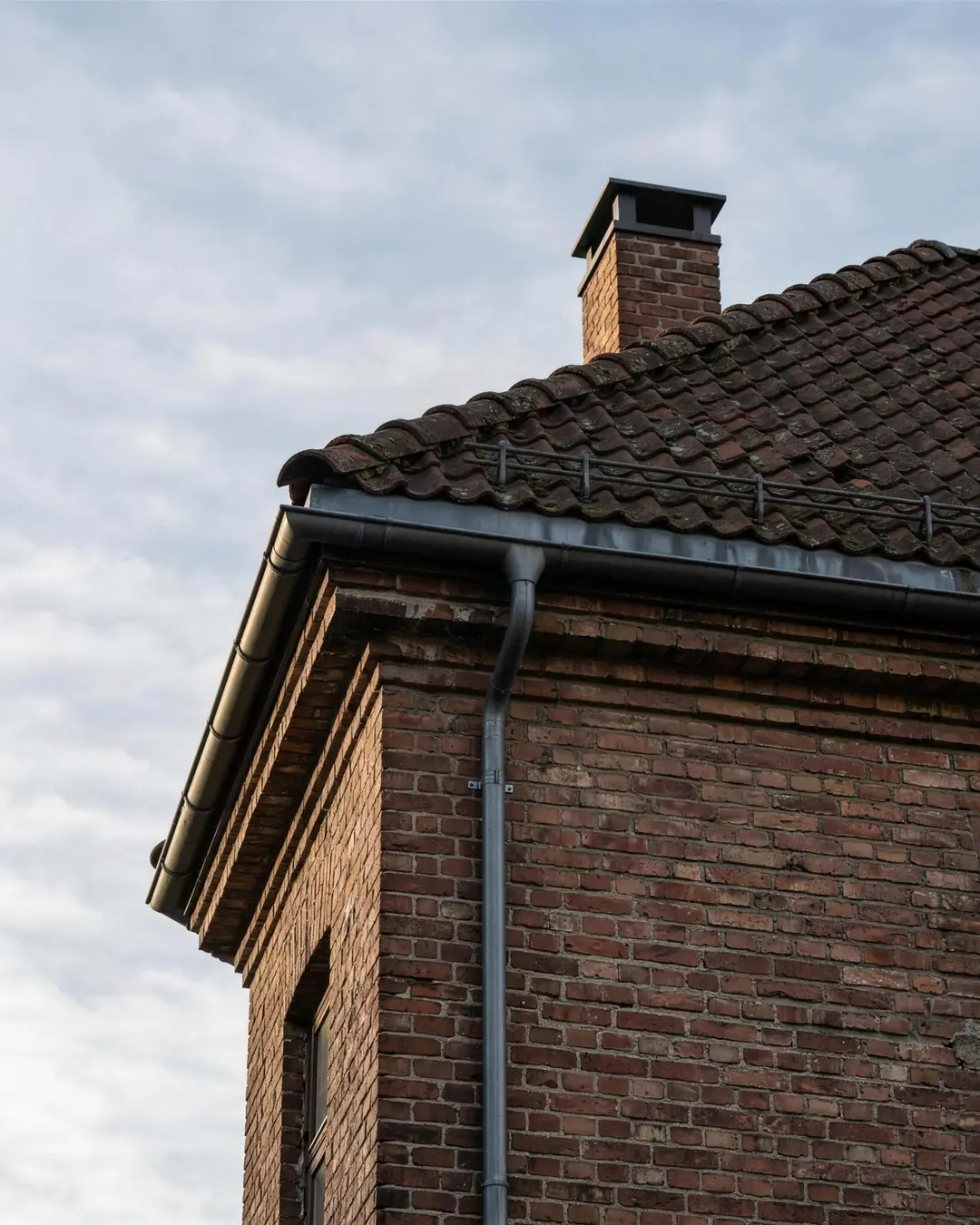 Nærbilde av takstein og takrenne på en eldre boligblokk, overskyet dagslys.